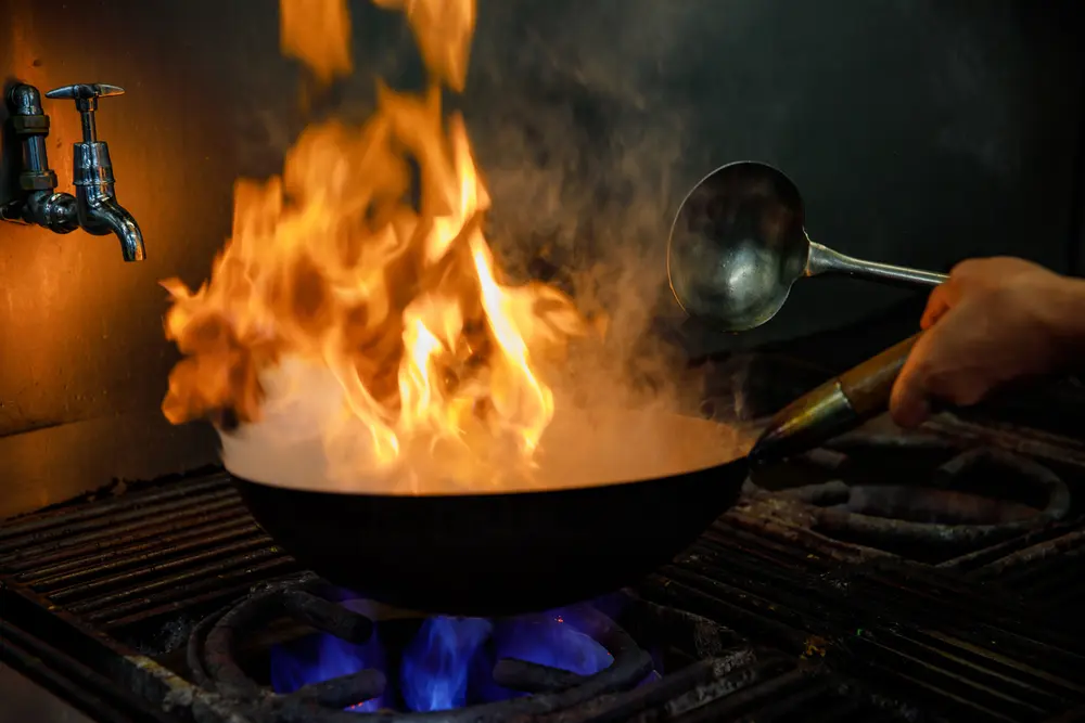 Chef flambéing food in a wok over a gas flame in a restaurant kitchen