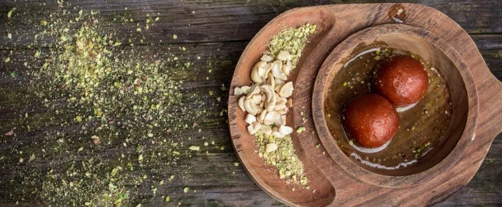 Gulab jamun sweets with cashews and pistachios on a wooden platter
