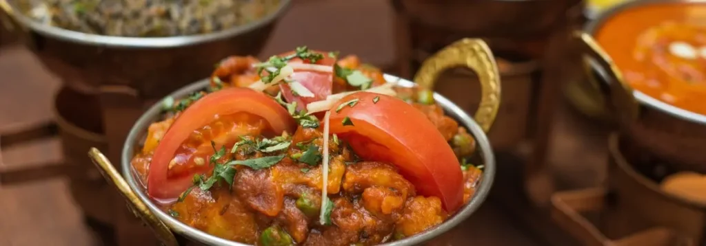 Indian curry with tomato wedges and herbs served in a copper karahi bowl