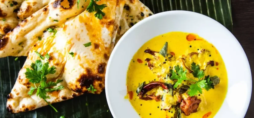 Bowl of yellow Indian curry with naan bread and coriander on a banana leaf
