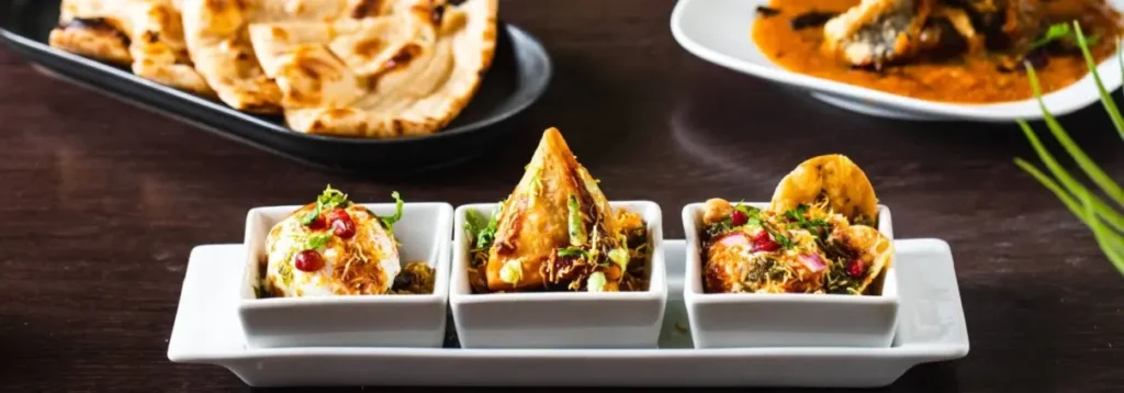 Assorted Indian side dishes including samosa and chaat with naan and curry behind