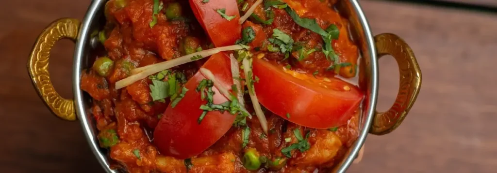 Indian tomato curry with peas, coriander and ginger in a karahi bowl