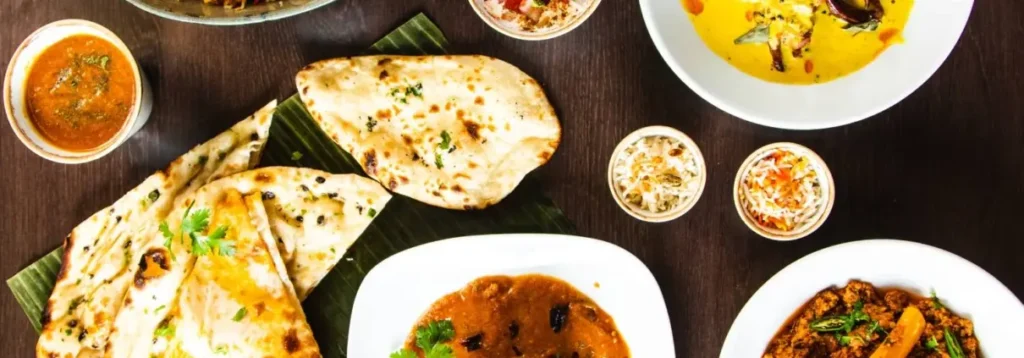 Assorted Indian wedding menu dishes including naan, curries, and side sauces on a dark wooden table