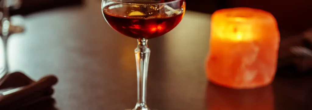A stemmed glass of amber cocktail with a glowing orange candle on a dark table at Itihaas Indian restaurant.