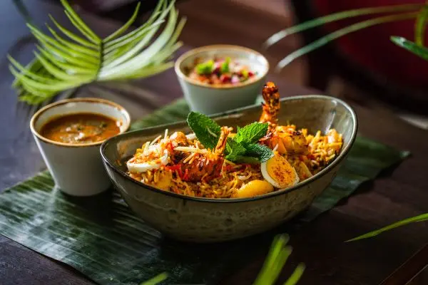 A steaming bowl of Itihaas spicy biryani garnished with mint, egg and chili, served with side sauces on a banana leaf.