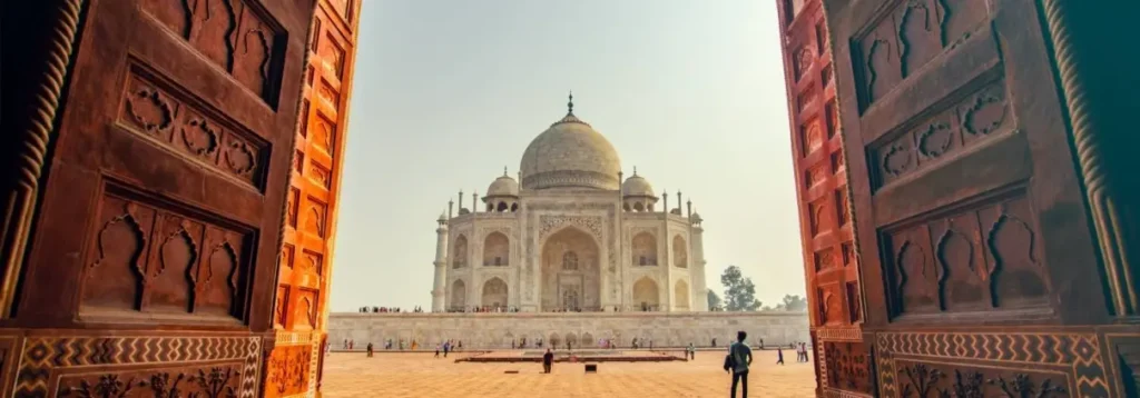 View of the Taj Mahal through carved wooden doors, showcasing the iconic white marble mausoleum in Agra, India
